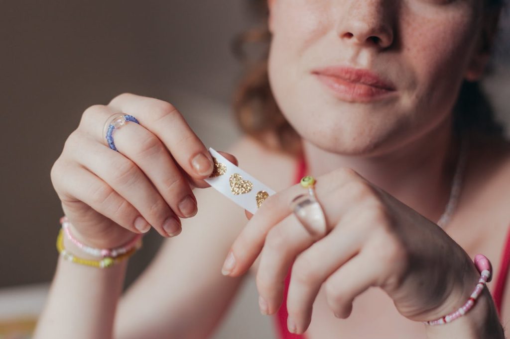 A woman with freckles holds gold heart stickers, showcasing jewelry details in a close-up.